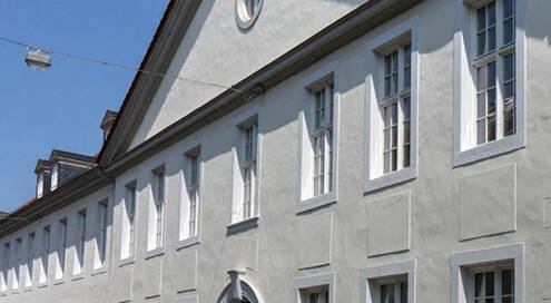 Gebäudefassade des ehemaligen Großen Waisenhauses. Viele Fenster mit weißen Rahmen, heller Anstrich. Klarer, blauer Himmel im Hintergrund