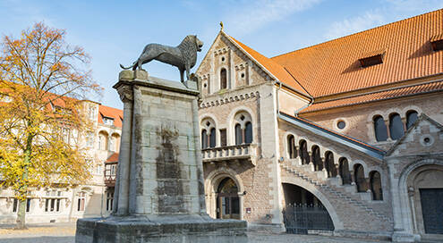 Burgplatz in Braunschweig mit Löwen-Statue und Burg Dankwarderode, im Hintergrund blauer Himmel.